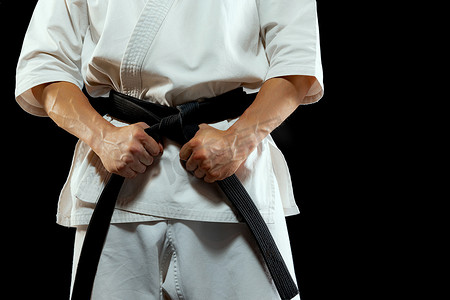 fighting摄影照片_Power and strength. Cropped image of male karate fighter in white kimono and black belt in fighting stance on dark background. Sport, action, combat sports, ad concept