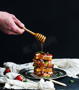 草莓塔摄影照片_法国吐司塔草莓、 奶油干酪和薄荷，手在它的顶部是浇注蜂蜜