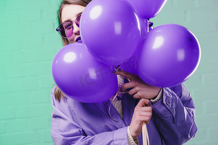 紫色气球摄影照片_戴墨镜的年轻女子躲在紫色气球后面