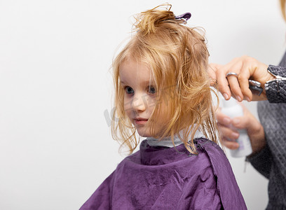 头发的切割过程。理发店里漂亮的小女孩，发型师给可爱的高加索4-5岁小女孩做发型