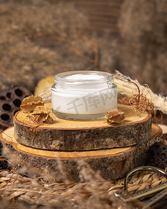 Opened glass cream jar on wood near natural decorations close up, package mockup. Eco friendly skincare product, lotion or cream. Bohemian composition with dried leaves and flower