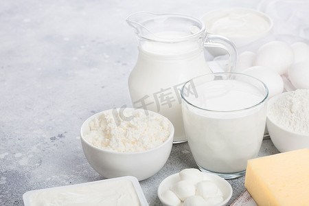 白色餐桌上的新鲜乳制品。罐子和一杯牛奶，一碗酸奶油，干酪和烤面粉和莫扎雷拉。鸡蛋和奶酪。文本空间