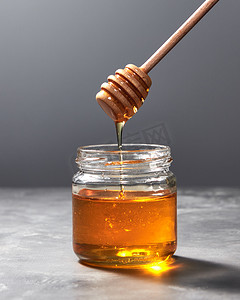 滴水有机天然新鲜蜂蜜从玻璃壶在灰色厨房石材背景与复制空间。犹太人犹太新年假日概念.