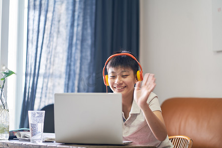 在网上上课的亚洲小孩笑着，头戴耳机