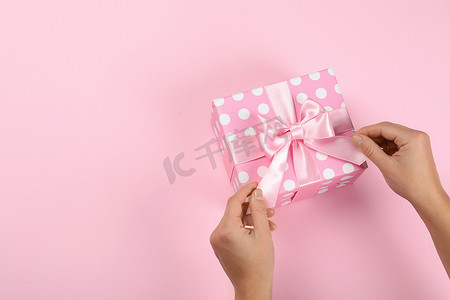 粉红蝴蝶结摄影照片_粉红背景的带蝴蝶结的女性手和礼品盒