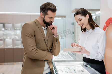 Smiling seller pointing at jewelry near focused customer in shop 