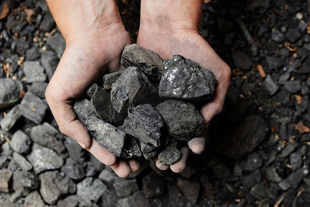 能源开采摄影照片_煤矿矿工在人手中的煤炭背景。煤炭开采或能源、环保。工业煤。火山岩.