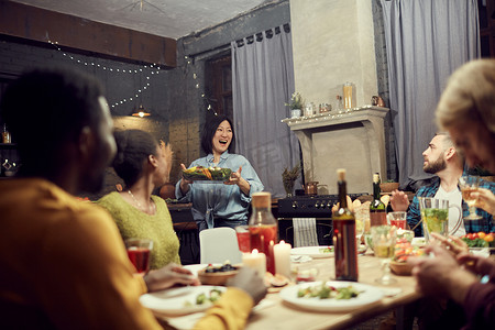 宴摄影照片_在与朋友举行的家庭宴会上，兴奋的亚洲女人带着主菜到餐桌前的肖像，复制空间