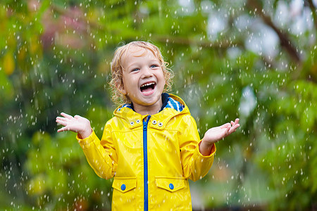 秋风秋雨摄影照片_孩子们在秋雨中玩耍。孩子们在雨天在户外玩耍。小男孩在大雨中雨点。公园里的秋天风暴。儿童防水服。任何天气下的户外儿童.