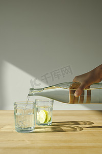 女人从瓶子里倒水到透明玻璃的裁剪图像 