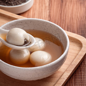 将芝麻大汤圆（汤圆，糯米团）与甜糖浆汤放在木碗里，放在木桌上，作为冬至佳肴.