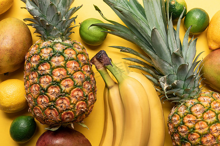 整个成熟的香蕉，菠萝，柑橘类水果和芒果在黄色背景的顶视图