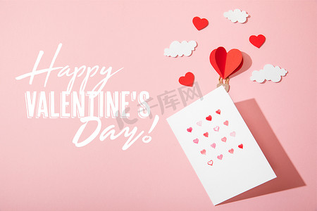 top view of greeting card with hearts near paper heart shaped air balloon in clouds and  happy valentines day lettering on pink