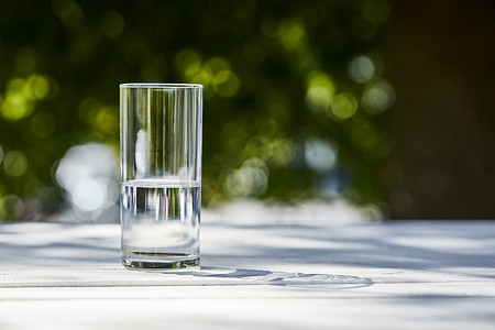 室外的木制桌子上，阳光明媚的日子，用透明的玻璃杯盛放清水