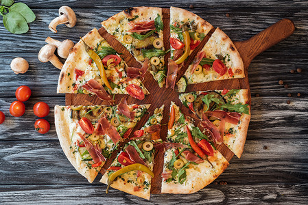 top view of sliced delicious pizza with vegetables and meat on wooden cutting board  