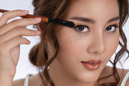 cosmetic摄影照片_Closeup gorgeous young woman putting black mascara on her long eyelashes with brush. Beauty cosmetic concept. Female model with perfect skin.