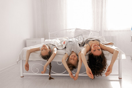 讲规矩守纪律摄影照片_快乐的家庭母亲、女儿和儿子在家里的白色卧室里玩得很开心。待在家里，守规矩.