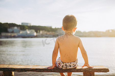男孩坐在板凳上背水附近的海滩上，显示他的手前进方向的背景下的基辅市.