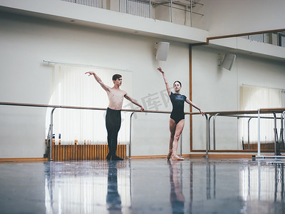 年轻的男子在古典芭蕾与年轻漂亮的女子在健身房或芭蕾舞厅黑色服装练习。情侣跳跳舞性感舞蹈。简约内饰,