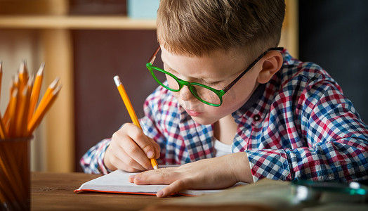 在学校第一次见到戴眼镜的快乐的笑脸男孩。孩子们呆在家里的房间里，房间里装着木制的背景。回学校去小男孩写信给空白。教育概念.