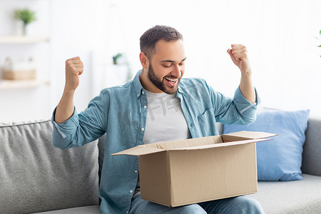 no和yes框摄影照片_Satisfied male client opening box, excited over delivery service, receiving online store order, gesturing YES at home