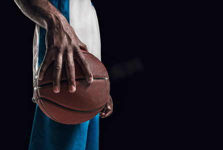 一个球在黑暗摄影棚背景下的篮球运动员之手。广告的概念