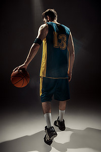 篮子球摄影照片_一名拿着篮子球在黑色背景上的篮球运动员的剪影视图