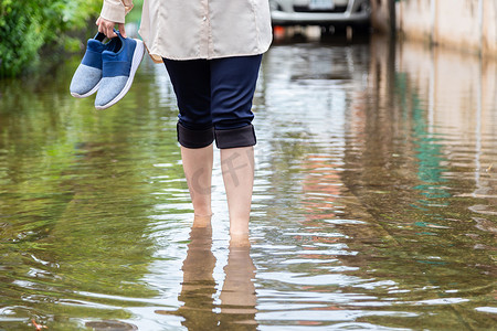 小心讨好摄影照片_大雨过后，女人在路上拿着鞋子行走，包括发痒的皮肤，要小心钩端螺旋体病，它可能会被水、运动员的脚或脚掌感染