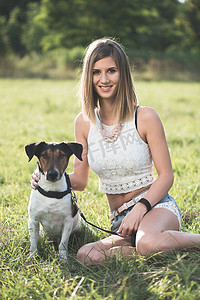 Blonde woman sitting with a cute terrier dog outdoor in the park.