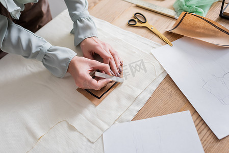 缝纫剪影摄影照片_裁缝师手持缝纫图案和粉笔靠近草图的剪影 