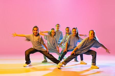 little摄影照片_Hip-hop dance, street style. Happy children, little active girls in casual style clothes dancing isolated on orange background in purple neon light. Concept of music, fashion, art