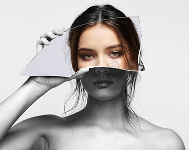 Girl covers her face with a shard of the mirror. Female with mirror shard in hand 