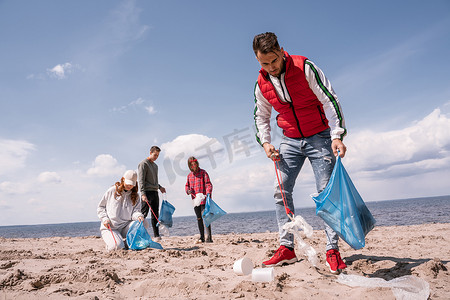 义工附近的年轻人提着垃圾袋，在沙地上捡垃圾 
