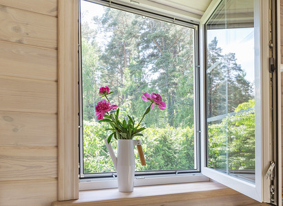 屋里的装饰摄影照片_白色的窗户,有蚊帐,在一座俯瞰花园的乡村木屋里.浇灌的粉红色牡丹花束可以放在窗台上