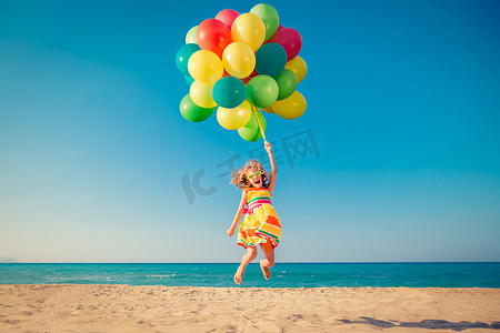 小孩跳摄影照片_快乐的孩子在沙滩上与五颜六色的气球跳