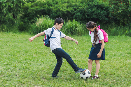 快乐的小学生一起在公园的草地上踢足球