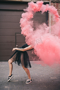 在城市街道的粉红色烟雾跳舞的灵活的年轻妇女  