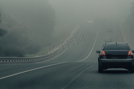 汽车摄影照片_大雾中的汽车在危险的天气行驶在高速公路上.能见度低，道路上的汽车交通状况差。高速公路上迷雾中的车辆