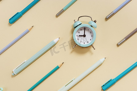 闹钟显示早上9点，该去学校上课了。用黄色和蓝色彩绘的钟表和固定学习用品进行创造性布局.