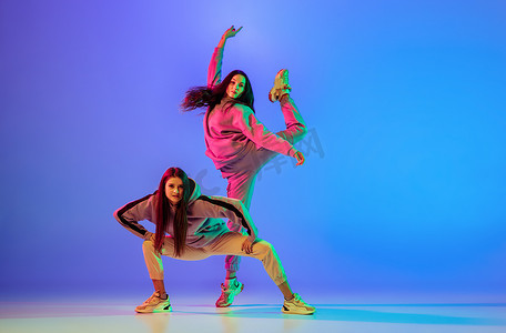 两个穿着休闲装的年轻漂亮女子跳着舞步舞，在霓虹灯下跃过蓝色的背景.