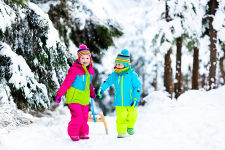 孩子们在雪地上雪橇在冬季公园玩耍