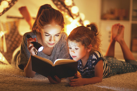 母亲和孩子的女儿阅读一本书和一个手电筒前
