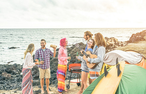 一群快乐的朋友庆祝喝啤酒和玩吉他, 而露营与帐篷冲浪者的乐趣听音乐在烧烤野餐户外-假期, 旅行生活方式的概念