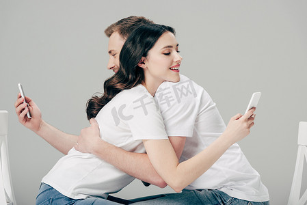 年轻男女在使用灰色智能手机时拥抱在一起