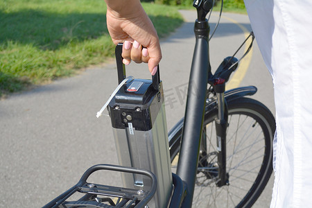 妇女在她的电动车附近手持电动自行车电池组。女性拿出电动自行车电池。生态学概念。充电电池。可再生能源. 