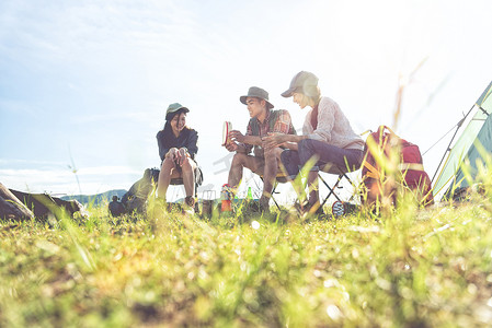 小组旅行者野营和做野餐在草甸领域前景。山和湖背景。人和生活方式的概念。户外活动和休闲主题。背包客和徒步旅行者主题
