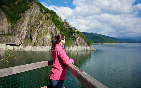 黑头发的女性游客望着远方, 欣赏着在罗马尼亚的绿色落基山脉和惊险的 Vidraru 湖的壮丽景色。美丽的风景风景愉快的安静的妇女