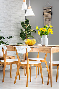餐厅内有白色的椅子和灯, 里面有水仙花和柠檬, 在一张木桌上的碗里。真实照片