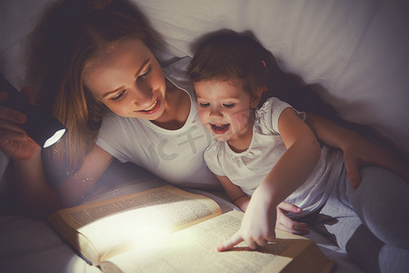 家庭阅读的就寝时间。妈妈和孩子读书与 flashl