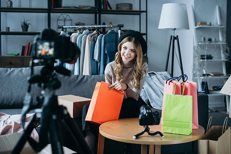 视频网摄影照片_微笑的时尚博客坐在购物袋和录制新的视频网 
